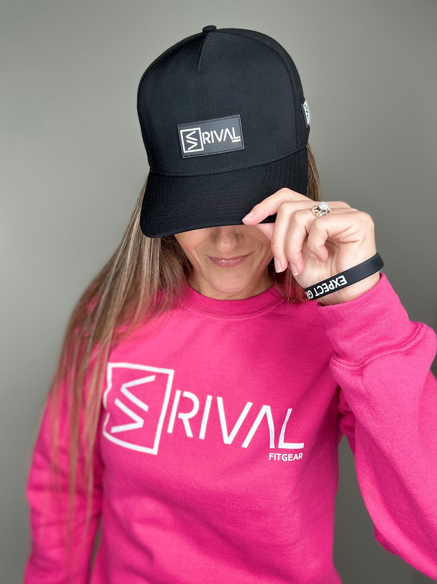 Female model tipping Rival Fit Gear hat and wearing bracelet and sweatshirt.