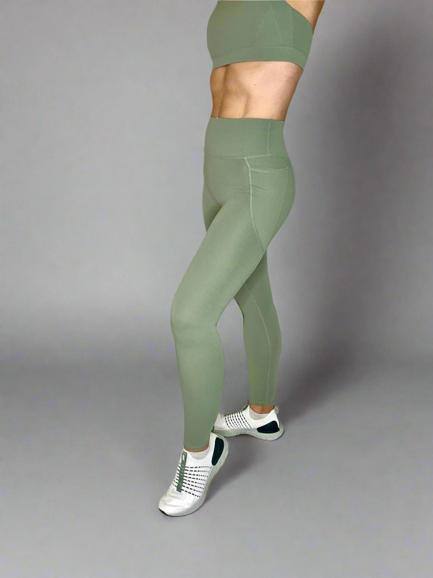 Model showcasing Rival Fit Gear Ignite Pocket Leggings in Moss side view.